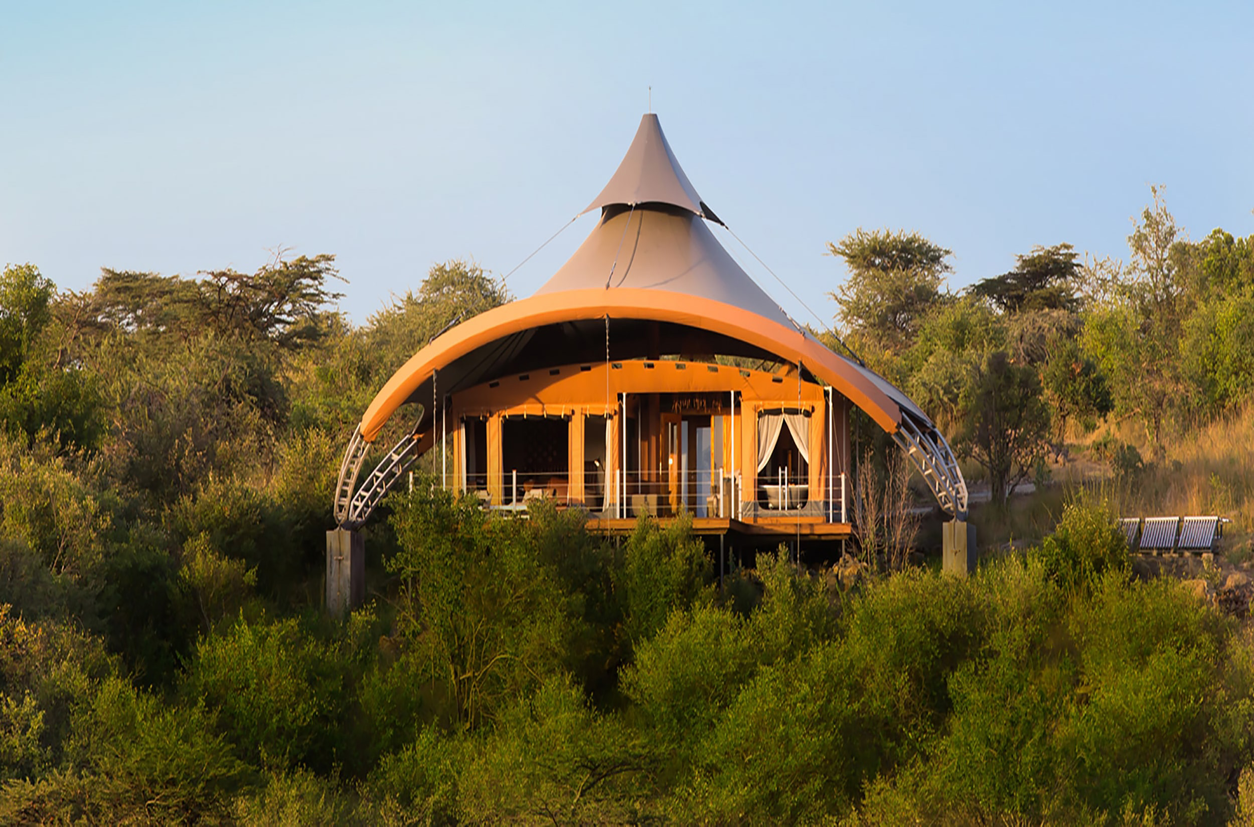Luxury tented safari camp deck with lanterns overlooking the Kenyan savannah at dusk