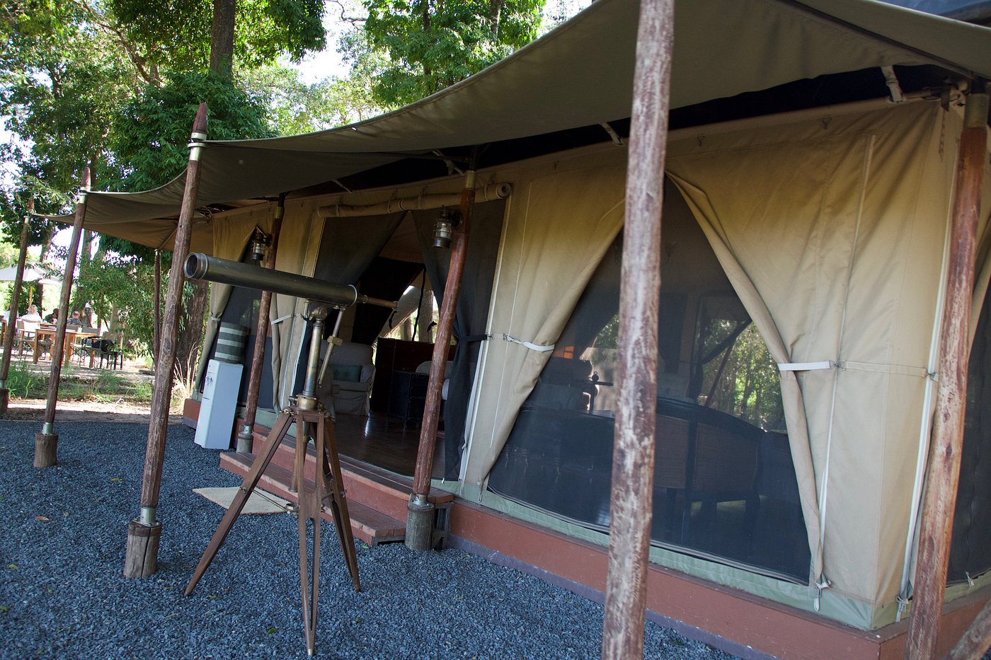 Canvas safari lounge tent with a telescope at Elewana Sand River Masai Mara camp under shady trees