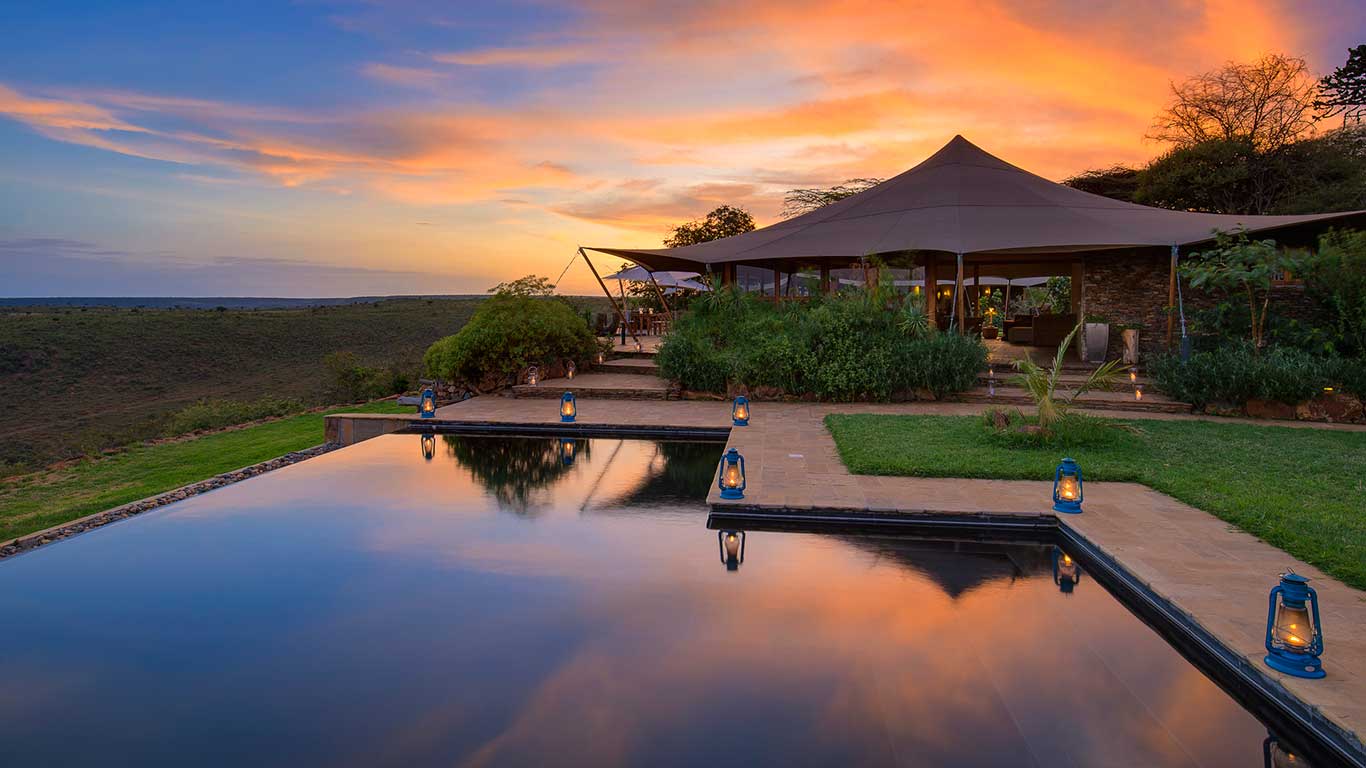 Tented safari lodge at sunset beside a reflecting pool, likely Elewana Loisaba Tented Camp, with open plains views
